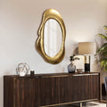 free form shaped gold color metal frame mirror on the wall, above a walnut sideboard with gold accent