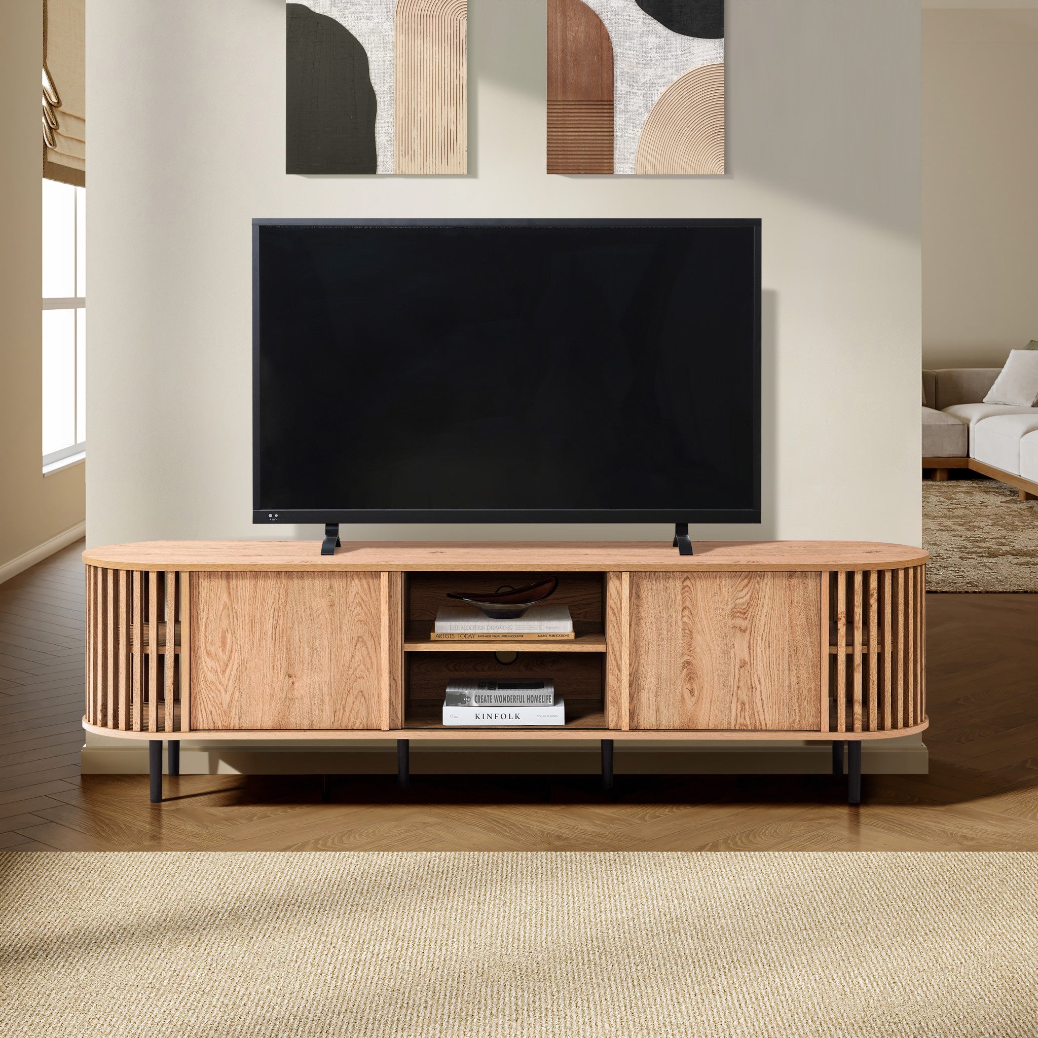 A mid-century modern TV cabinet with a flat-screen TV sits on a wooden stand with shelves, holding books. Its set against a living room wall adorned with abstract art, perfectly complementing the sleek sliding door design nearby.