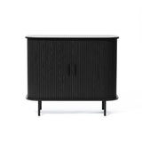 The Aria accent cabinet in a black finish is a stylish Mid-Century Modern piece with vertical grooves. It features a rounded top, stands on four sleek legs, and includes two push-to-open doors.