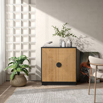 A contemporary living room features a geometric-patterned cabinet, potted plants, natural bamboo strips accenting the decor, and a leaning framed artwork beside a chair on a textured rug.