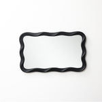 Modern wall mirror featuring a wavy black frame adds a stylish touch, beautifully mounted on a white wall.