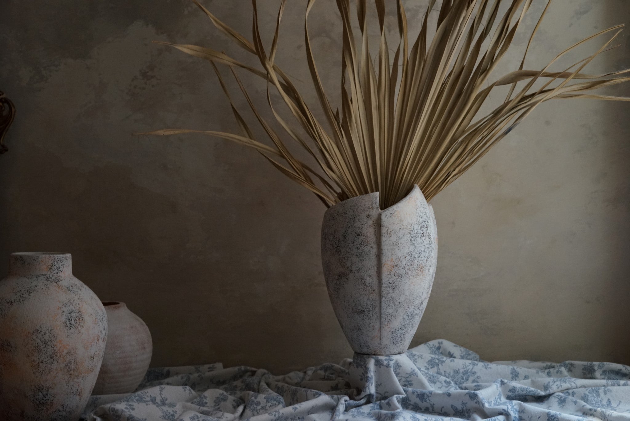 vintage like weathered finish crack open ceramic vase with dried tropical leave in low light environment by the window