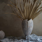 vintage like weathered finish crack open ceramic vase with dried tropical leave in low light environment by the window