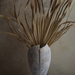 cracked open antique marble-like finish terracotta vase with dried tropical leaves inside