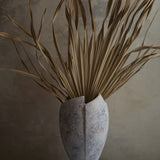 cracked open antique marble-like finish terracotta vase with dried tropical leaves inside