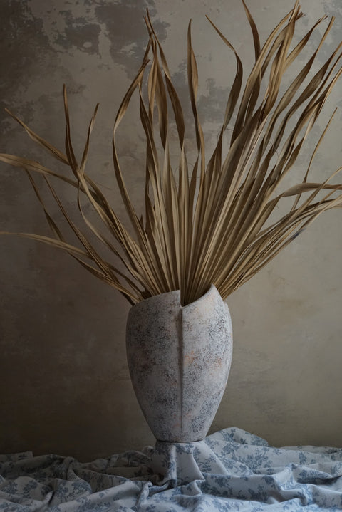 cracked open antique marble-like finish terracotta vase with dried tropical leaves inside
