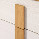 Close-up of a wooden handle on a nightstands white drawer with visible grain patterns, showcasing its refined wooden finish.