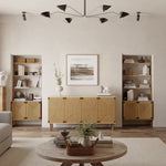 A living room embodying natural modernism features a ceiling light fixture, two bookshelves, and a central wooden cabinet with jute-woven doors. A round coffee table and neutral decor complete the look, with framed art, vases, and versatile storage solutions adding to the aesthetic.