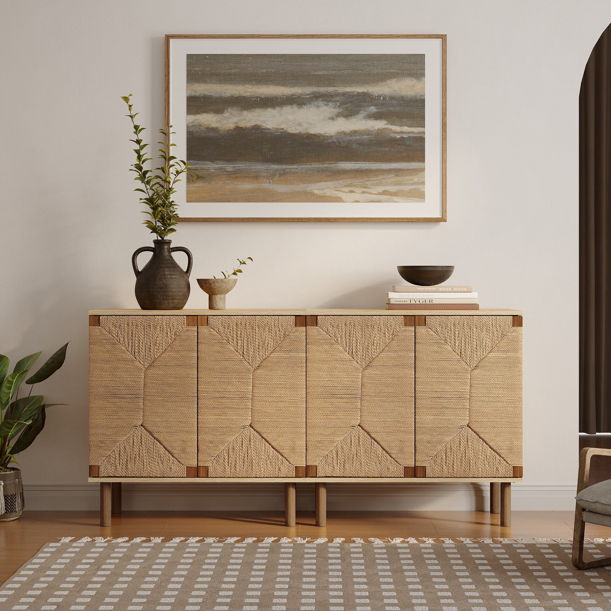 A woven wooden sideboard with jute-woven doors sits beneath a framed abstract ocean painting. Decor includes vases with greenery, a bowl, and books, reflecting natural modernism. The room is completed with a patterned rug and a partially visible chair.