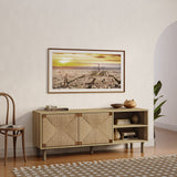 A framed cityscape photo hangs on a wall above a sleek, mid-century modern sideboard with woven-front detailing and curated decor. A chair stands next to the sideboard, and a patterned rug covers the floor.