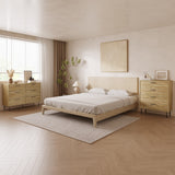 A minimalist bedroom showcases a wooden bed, beige bedding, and two wooden dressers. The LuxenHome Casper mid-century modern 4-drawer chest with metal legs adds elegance beside a potted plant. A textured rug covers the floor under natural light from a large window. Neutral art decorates the wall.