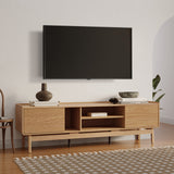 A modern living room showcases the LuxenHome Eric oak finish 70 TV stand, holding vases and books. A flat-screen TV mounts above it. The patterned rug adorns the hardwood floor, with a wooden chair partially visible on the left.