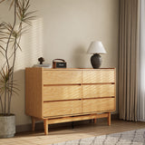 The LuxenHome Eric oak finish 6-drawer dresser stands against a beige wall topped with a vintage radio, dark vase, and white lampshade. Nearby is a tall potted plant, with curtains partially covering the window on the right. This Mid-Century Modern piece adds timeless charm to the room.