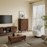 In a cozy living room, a modern wood TV stand accompanies a large flat-screen TV. A LuxenHome Theo mid-century modern walnut finish 5-drawer chest complements the setup. Nearby, a white swivel chair is by the window with sheer curtains, and decor pieces adorn a wooden coffee table on the beige carpet.