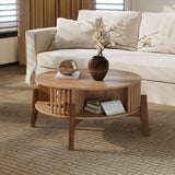 A cozy living room features a white sofa and the LuxenHome Miko coffee table with solid wood legs. The table holds a ceramic vase with blooming branches, a small bowl, and an open book on its lower shelf. The room exudes neutral tones on a woven carpet.