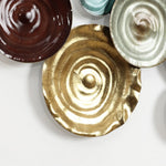 A decorative wall display showcasing abstract design with overlapping metallic plates in gold, brown, and silver hues, each featuring a textured concentric circle pattern. This captivating piece of metal wall art adds depth and elegance to any space.