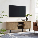 A minimalist living room features a LuxenHome Aria oak finish 55.1 TV stand nestled beneath a wall-mounted flat-screen TV. The console, storing electronics discreetly, is topped with a bowl and plant. A large window illuminates the space naturally as a brown sofa edges into view.