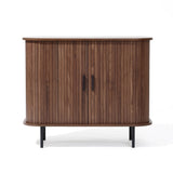 The Aria by LuxenHome is a Mid-Century Modern accent cabinet featuring tambour doors and two black metal handles. It boasts a dark oak finish with a curved front atop four slender black legs, enhancing its elegant design.