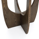 A dark wooden abstract sculpture with geometric cutouts stands on a white surface, echoing the sleek elegance of a mid-century modern side table.