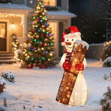 A snowman outdoor holiday decoration with a Santa hat and scarf holds a large ruler labeled LET IT SNOW in a snowy yard, with a decorated Christmas tree, lighted display, and festive house in the background.
