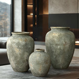 Three large LuxenHome rustic gold and brown terracotta urn vases, each 13.6 high, sit on a stone-textured table. With antique distressing for a weathered finish, they enhance the modern interior’s soft lighting and window view, creating an inviting decor statement.