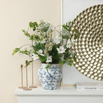 A white and blue floral ceramic vase holding a bouquet of white and green flowers is placed on a mantel.