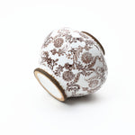 A white ceramic vase with intricate brown floral patterns, positioned on its side against a plain white background.