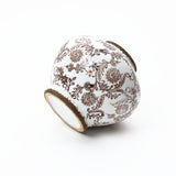 A white ceramic vase with intricate brown floral patterns, positioned on its side against a plain white background.