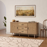 Buffet cabinet sideboard, a mid century storage cabinet with three drawers and two cabinets, placed against a white wall below a framed landscape painting, with a rug, chair, and potted plant completing the room scene.