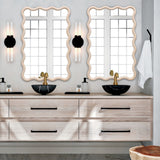 Modern bathroom with two black sinks, gold faucets, and wave-edged decorative wall mirrors. Pine wood finish cabinetry with dark handles and wall-mounted lights create a warm ambiance. White tiled windows provide a crisp backdrop.