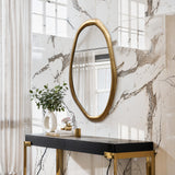 An elegant oval wall mirror with a gold frame adorns the marble wall above the black console table. A sleek white vase holding a green plant, accompanied by tasteful decorative items, graces the table, while light curtains draw softly from the left.