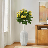 A LuxenHome modern geometric pattern resin tall trumpet vase, 23.5 h, holds a bouquet of vibrant yellow flowers with lush green leaves, placed on a wooden floor next to a cabinet with geometric leaf-patterned artwork in natural light.