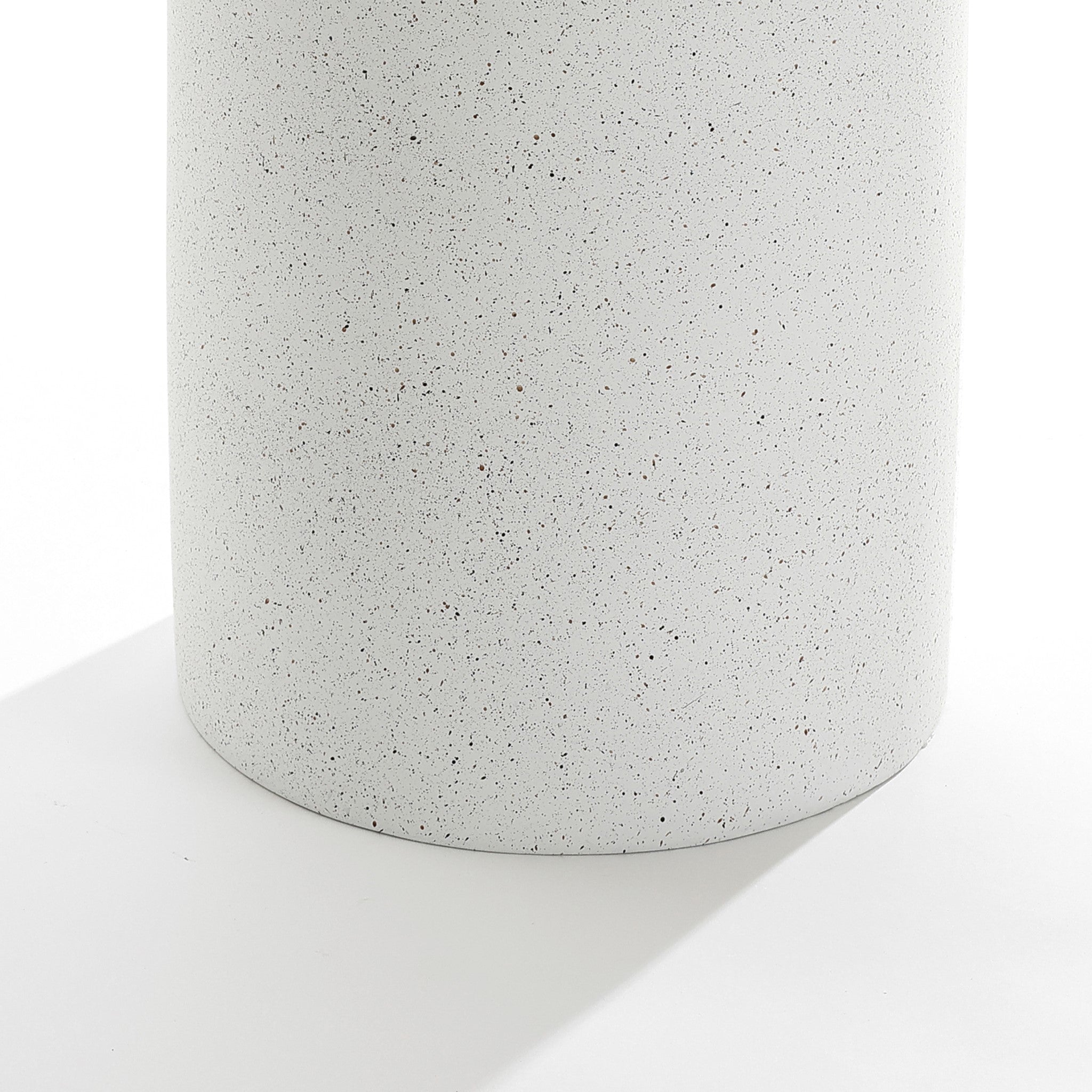 A close-up of the Speckled white pillar outdoor side table reveals its white, speckled surface. Made from durable MGO material, it features a smooth texture that casts a soft shadow, adding contemporary flair and making it perfect for modern outdoor settings.