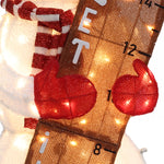 A close-up of a Snowman Outdoor Holiday Decoration with red mittens, a striped scarf, and a ruler marked with numbers, all illuminated by string lights—perfect as festive yard holiday decor.