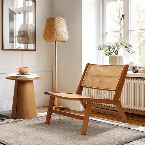 a low-profile accent chair made with wood and rattan sitting by the side of a rattan floor lamp and wood end table in a living room set up