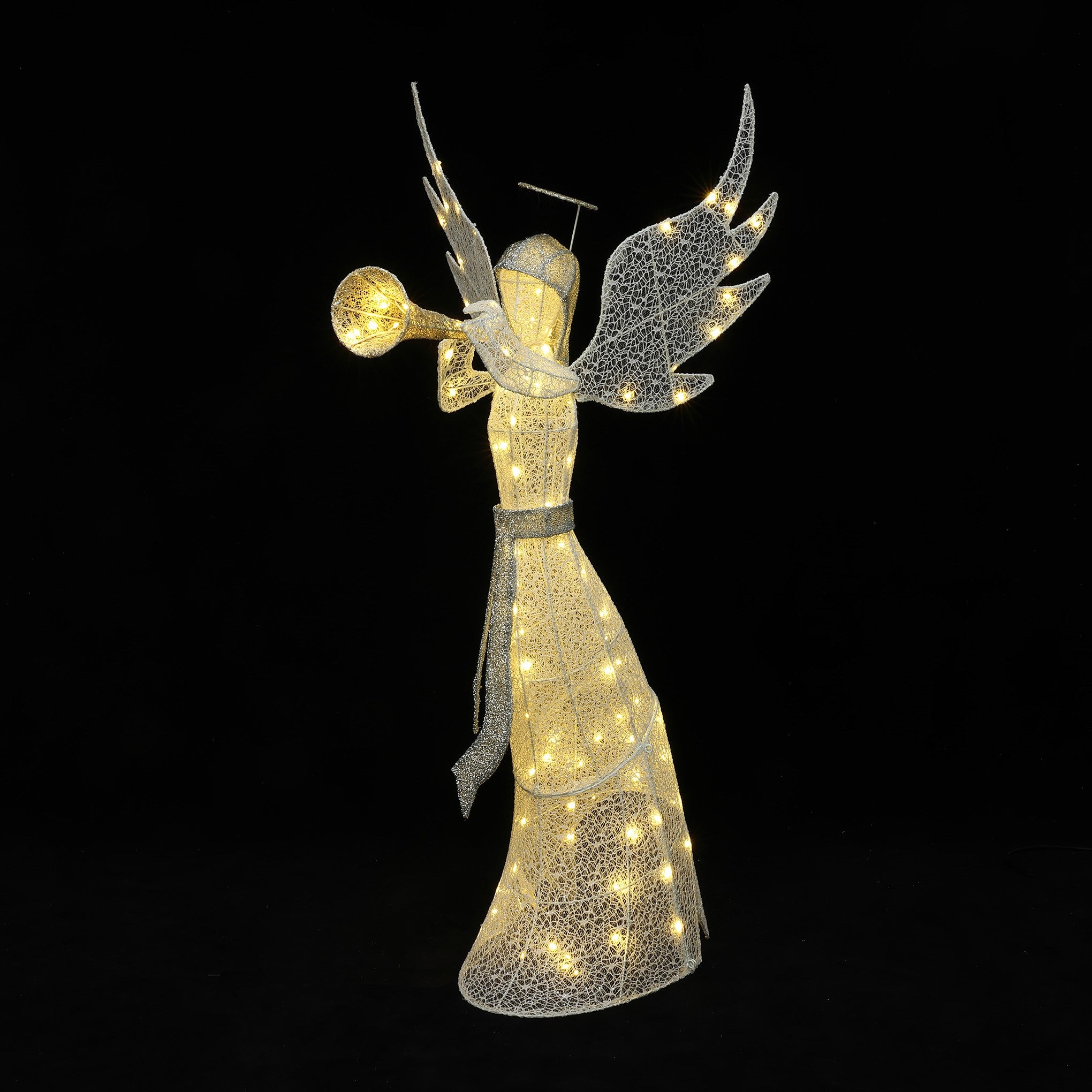 Pre-lit angel holding a trumpet stands in the snow outside,surround by illuminated trees ,lanterns.