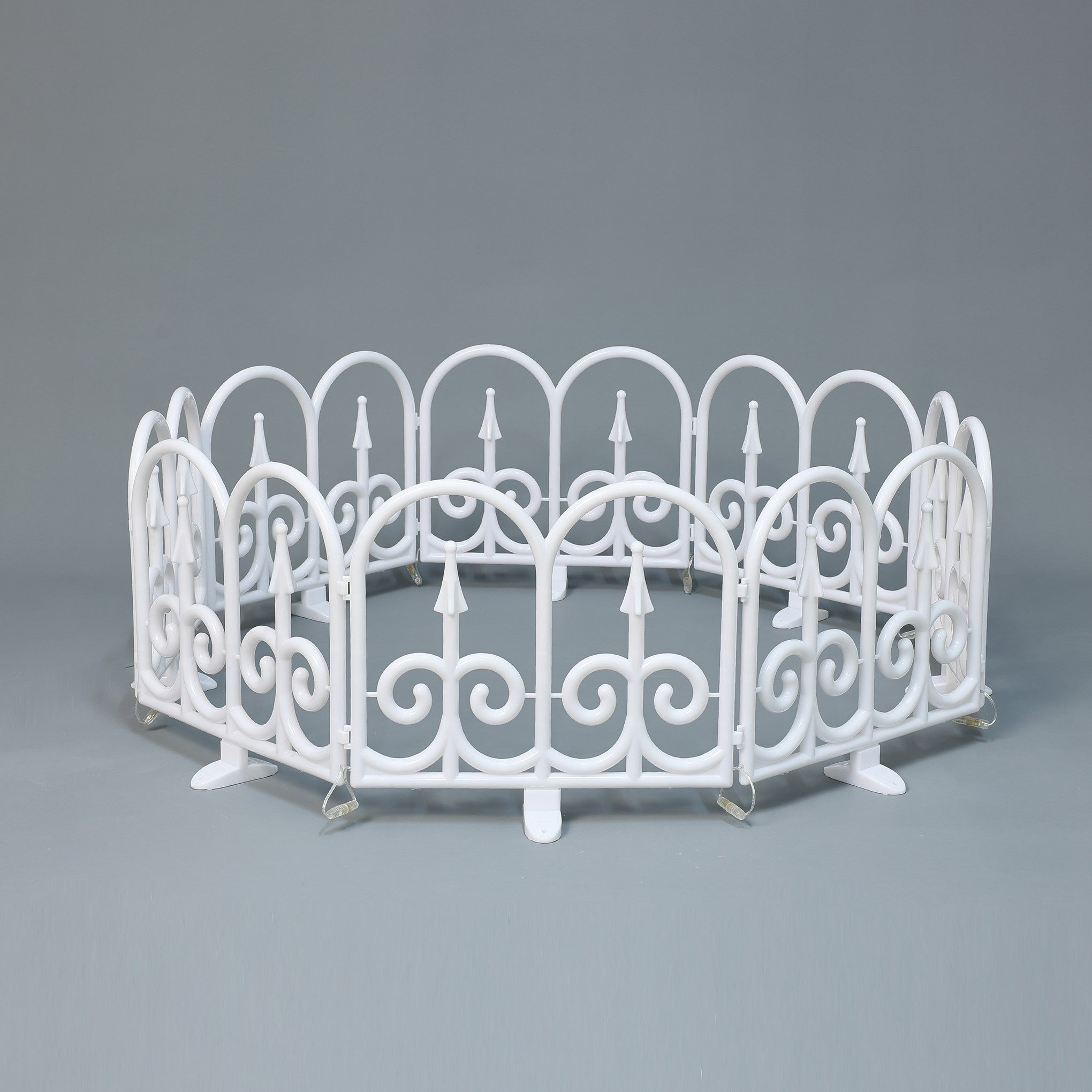 Small white circular fence with decor scroll ,pointed designs, against plain gray background.