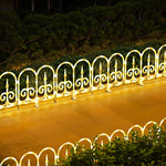 White decor led fence with bright yellow lighting stands on glossy surface,green bushes ,trees in background.