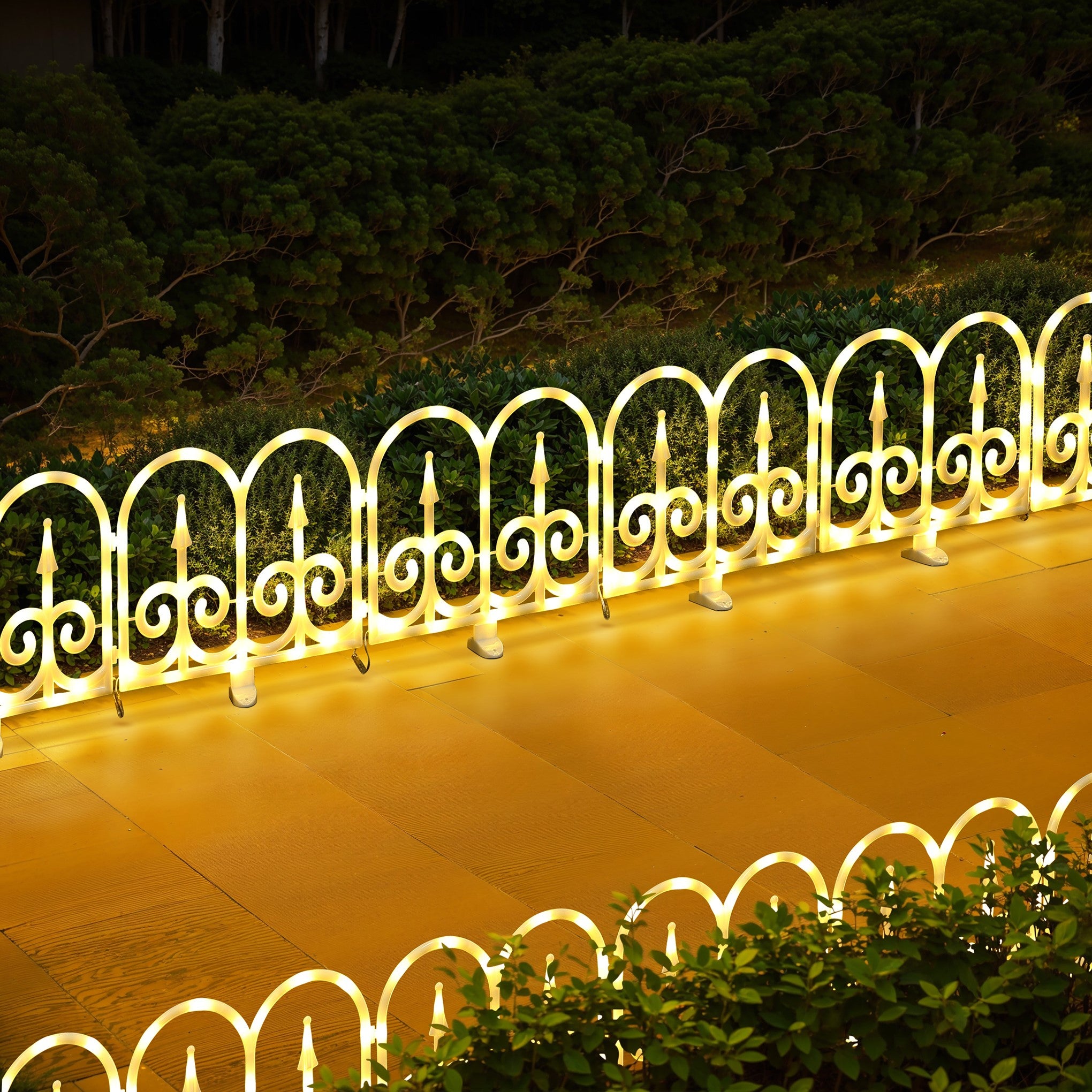 White decor led fence with bright yellow lighting stands on glossy surface,green bushes ,trees in background.