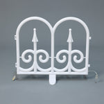 White plastic decor led fence piece with 2 arched tops ,swirl, standing upright against a plain gray background.