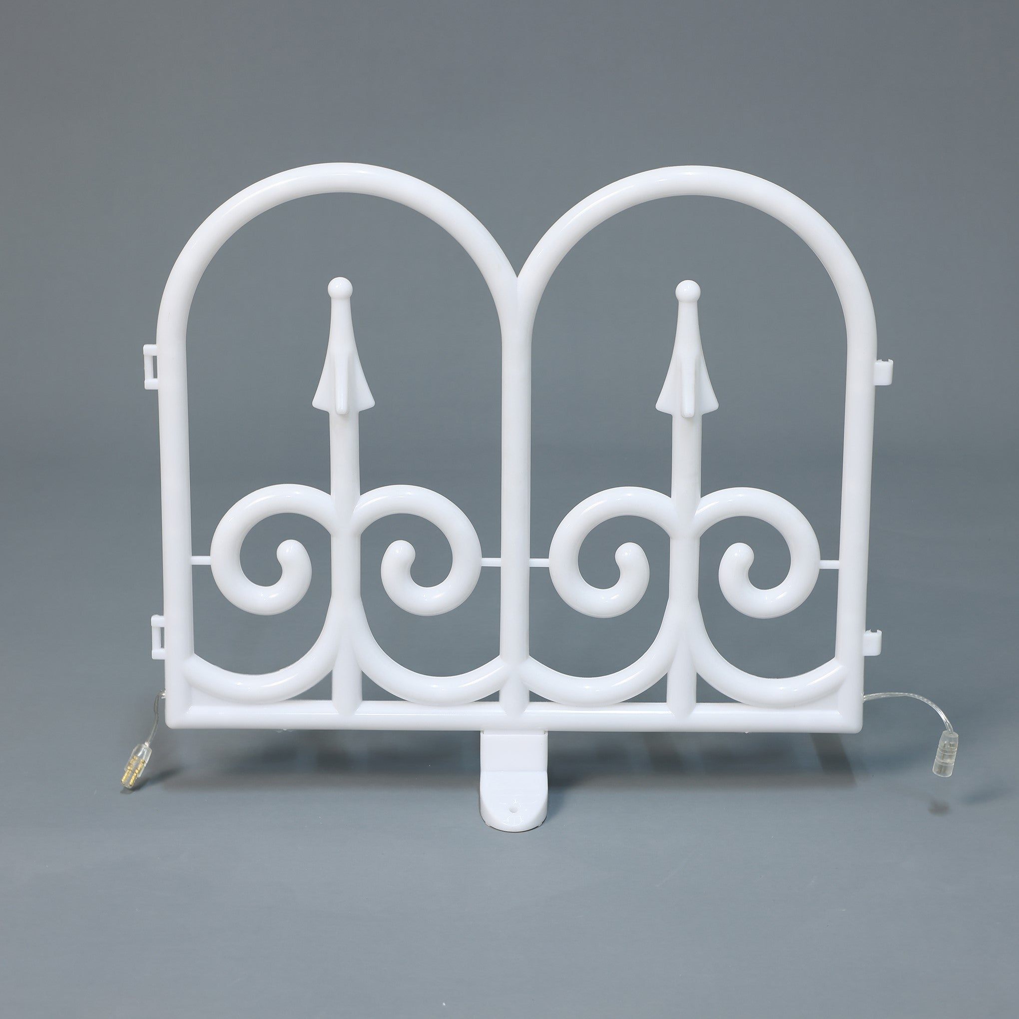 White plastic decor led fence piece with 2 arched tops ,swirl, standing upright against a plain gray background.