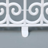 Close-up of white plastic fence segment with decor swirl design,flat base, displayed on a gray surface.