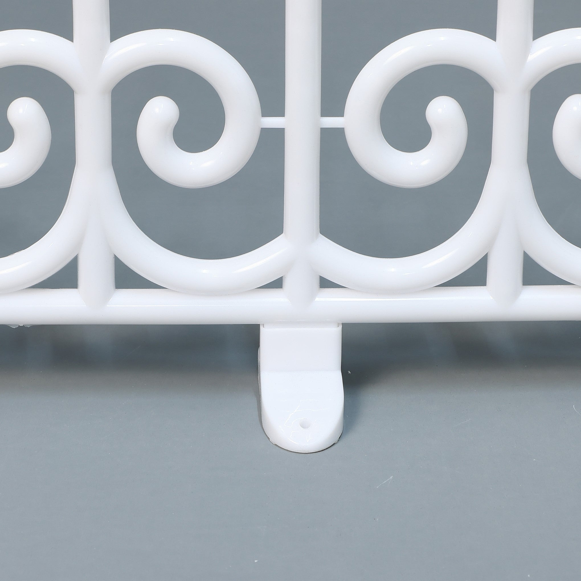 Close-up of white plastic fence segment with decor swirl design,flat base, displayed on a gray surface.