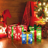 Three illuminated LED gift boxes with snowflake patterns sit beside a Christmas tree, surrounded by wrapped presents.