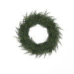 Artificial wreath made of pine branches forms circular holiday decor, against a plain white background.