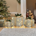3 pre-lit holiday decor gift boxes with gold ribbons, pine accents are displayed near Christmas tree ,nutcracker.
