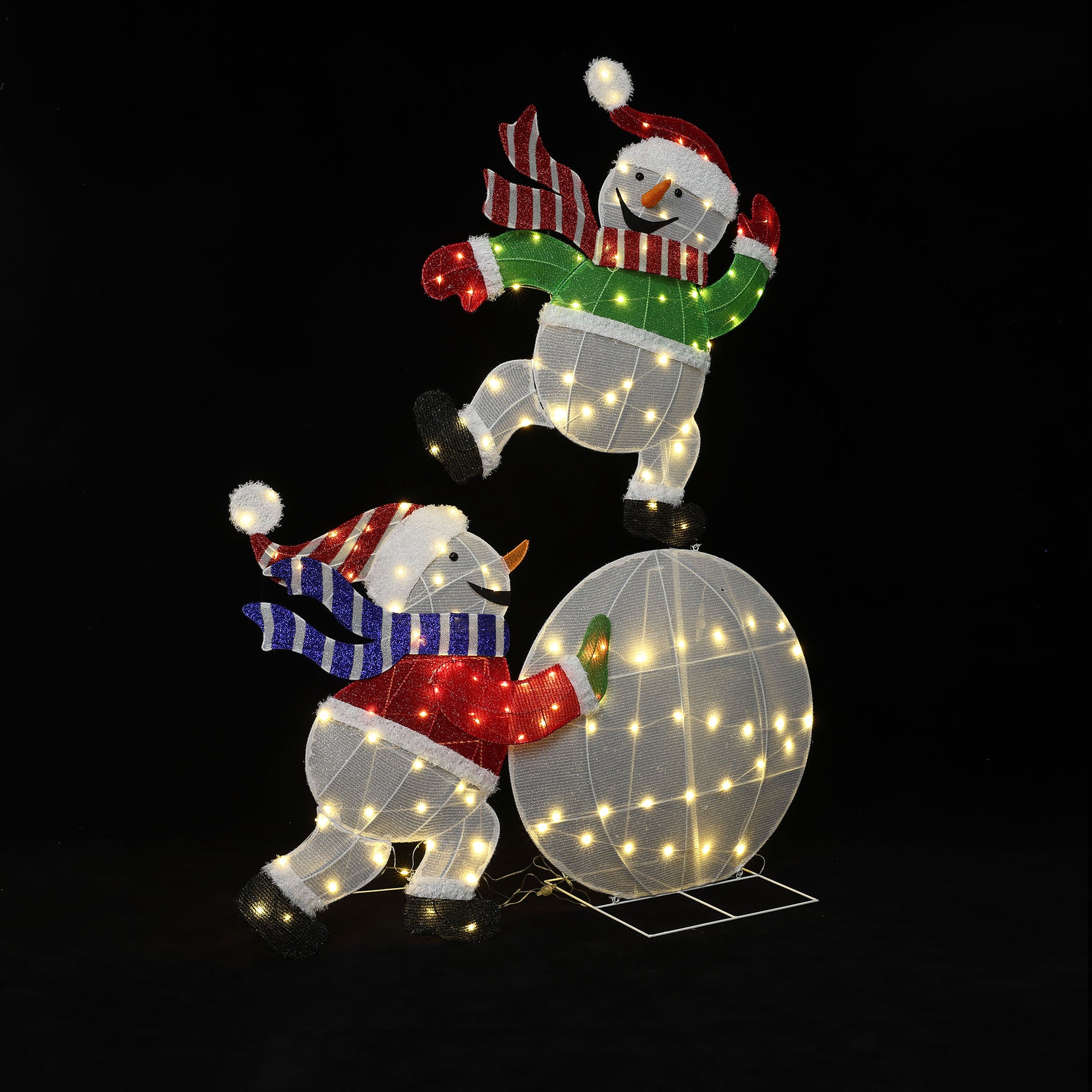 2 pre snowman holiday decor pieces, one with a red scarf , the other with green, balance playfully on a lit globe.