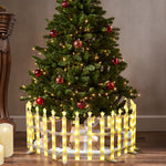 Christmas tree with white lights,red ornaments stands behind fence,wrapped gifts underneath,candles nearby.