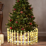 Christmas tree with white lights,red ornaments stands behind fence,wrapped gifts underneath,candles nearby.