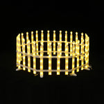 Round, white picket fence is illuminated with yellow star-shaped lights, set against black background.